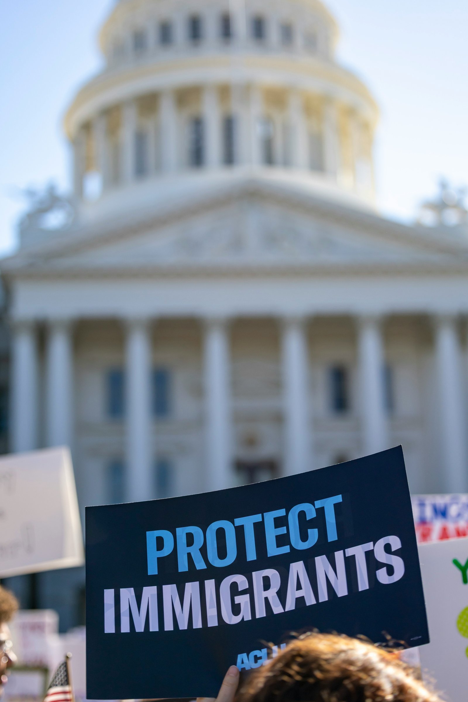 A sign reading Protect Immigrants held in front of a civic building.